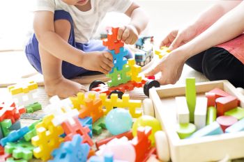 Kind und Erzieherin spielen mit bunten Stecksteinen