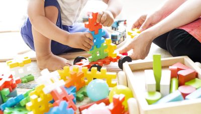Kind und Erzieherin spielen mit bunten Stecksteinen